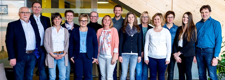 Das Team der Kanzlei Allertseder, dreizehn Personen nebeneinander vor der Holztreppe